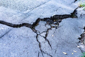 Cracked asphalt road surface damaged by landslide, showcasing deep fissures and uneven terrain,...