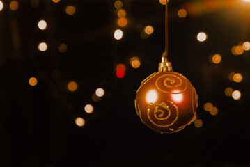 A warm, reddish-gold Christmas ornament with glitter spirals, hanging against a dark background...