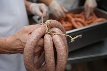 Hands tying rope around sausage links during the food preparation process in a kitchen.