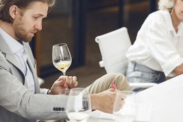 sommelier tasting white wine and making notes to degustation card during wine expert training.