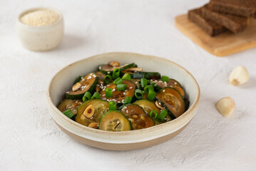 Cucumber salad with sesame seeds, green onion, soy sauce, garlic in a bowl with pieces of bread on a light table.