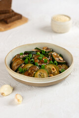 Spicy cucumber salad with sesame seeds, green onion, soy sauce and garlic in a bowl with slices of bread. Vertical orientation.