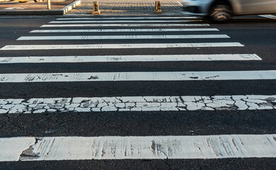 A worn pedestrian crossing with a vehicle speeding past. Motion, blur. Traffic sign.