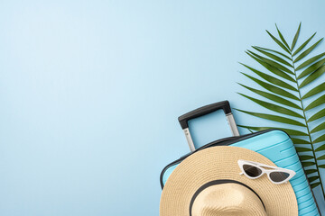 Travel essentials arranged, including a suitcase, sunhat, sunglasses, and a tropical green leaf,...