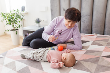Grandmother entertaining baby with toys on bed. Baby care.