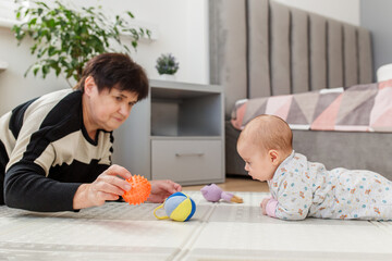 Grandmother engaging baby with toys during tummy time. Baby care.