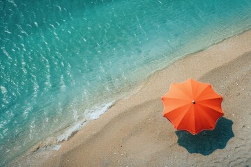 Bright orange umbrella on sandy beach beside clear blue water on a sunny day