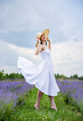 Beautiful brunette young woman In white dress and straw hat  relaxing in lavender field on summer...