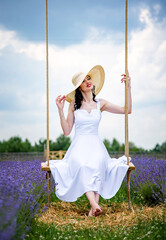Beautiful brunette young woman In white dress and straw hat  relaxing and swinging in lavender...