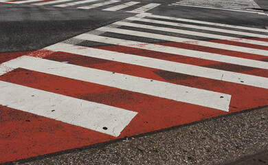 Pedestrian crossing in a street. White lines on the red and gray asphalt road background.