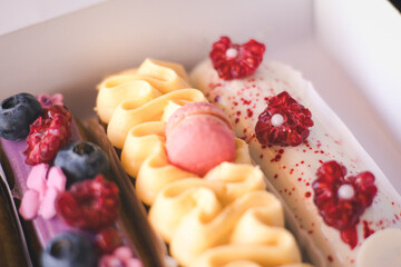 Delicious eclairs with fresh berries and macarons beautifully displayed in a bakery box. Colourful eclairs, adorned with fresh berries Creamy frosting