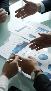 High-angle video: diverse hands, smart casual cuffs, various skin tones, interacting with business documents, charts, schematics on a modern conference table. Pen, pointing, agreeing gestures. Slow
