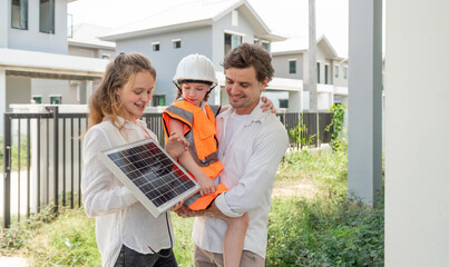 In a vibrant outdoor setting, a family examine a solar panel while a child dressed in safety gear...