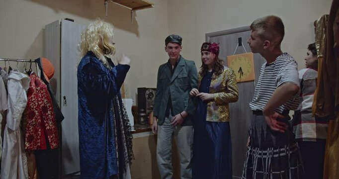 Actors in costume backstage at the theater, preparing for a performance. They chat, laugh, and rehearse their lines.