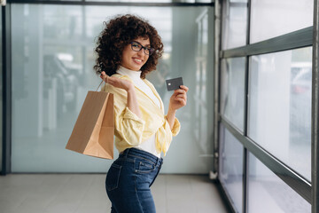 Shopping time, with credit card. Beautiful woman is standing indoors against blurred wall