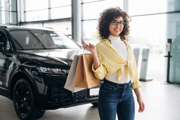 Customer is with shopping bags. Pretty woman is in the car retail shop