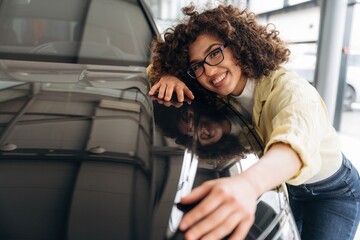 Embracing the car. Pretty woman is in the car retail shop