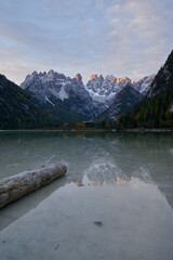 mountain landscape with lake and a tree trunk in the foreground at sunrise in the dolomites