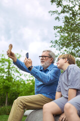 Teach the shot. Grandfather teaches boy to take picture of ice cream with smartphone. Concept of...