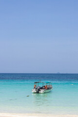 Small boat parks on the shore of Redang Island with crystal clear water with white sand