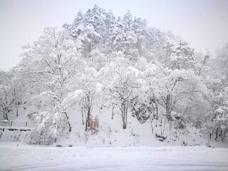 Snow-covered traditional Japanese village in Shirakawa-go style, with thatched-roof houses, trees, and mountains blanketed in deep winter snow