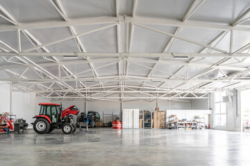 Agricultural machinery and storage area in modern industrial warehouse with tractor, shelving, cardboard boxes and tools. Farming, logistics, facility and transportation niches.