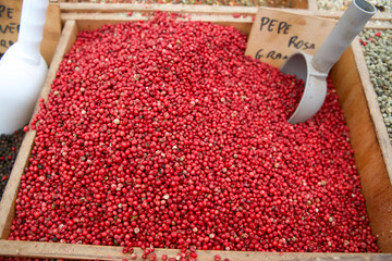 Red peppercorns displayed in wooden box at market with scoop and labeled sign indicating variety...