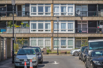 A council block building with balconies, alongside a street lined with parked cars in London