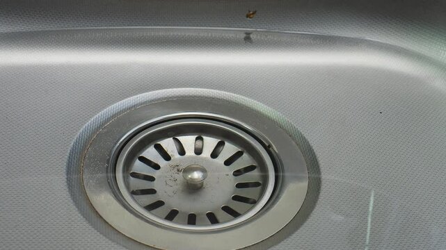 Clean water pours uselessly into a metal sink in the kitchen close-up waste of water
