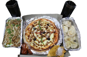 A whole pizza with a rich drizzle, a container of savory noodles  and a serving of steamed dumplings. Accompanied by two dark beverages and two dark beverages and sauces.
