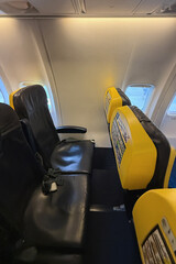 The interior of an airplane with black leather seats and yellow backrests with a missing window