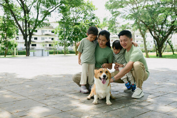 A cheerful family of four enjoys a sunny day in the park with their adorable Corgi dog, sharing...