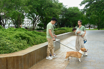 A Young Asian Family strolls with pet dog in peaceful green park, creating memories and bonding...