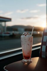 Classic strawberry milkshake with whipped cream in retro diner at sunset