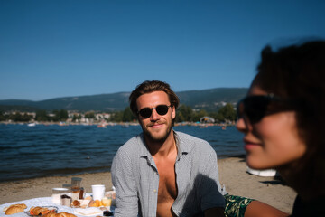 Young man smiling at beach picnic on summer day with mountains and lake in background