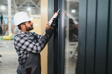 Indian worker is applying polyurethane foam to fill gap between sash and window frame in...