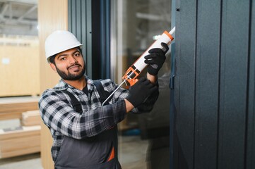 Indian worker is applying polyurethane foam to fill gap between sash and window frame in...
