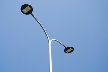 Modern double-headed street lamp with minimalistic design against a clear blue sky. Urban infrastructure detail on a bright sunny day. Concept of city lighting and outdoor public utilities.