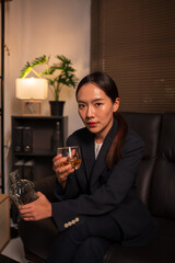 Businesswoman holding a glass of whiskey, sitting and drinking in a room