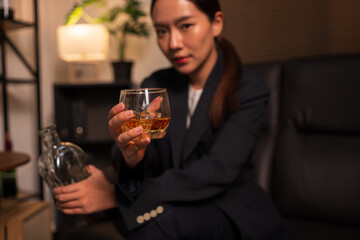 Businesswoman holding a glass of whiskey, sitting and drinking in a room