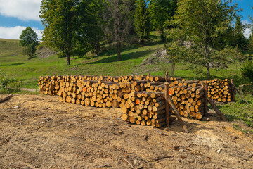 Large piles of freshly sawn timber are stacked on a clearing in a hilly forest area. Surrounded by...