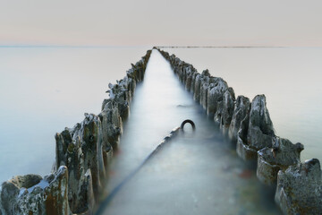 Twilight falls on weathered groynes leading into the calm sea, captured with a long exposure.