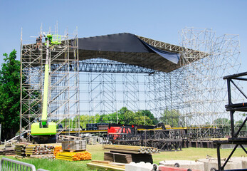 Stage construction for an outdoor concert. Workers on a lift and scaffolding are assembling the...