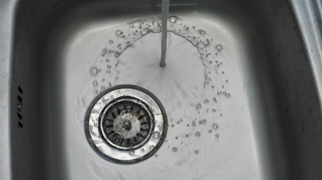 Clean water pours uselessly into a metal sink in the kitchen close-up waste of water