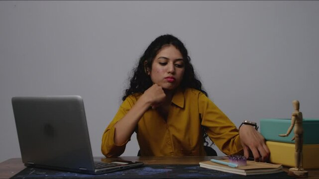 A drained and bored South Asian woman holding her phone in the office, staring blankly during an unmotivated work moment