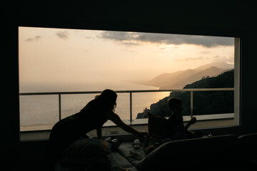 Fototapeta premium Family enjoying golden sunset over the sea from panoramic window in modern apartment