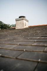 Chimney emerging from dark slate roof tiles under blue sky