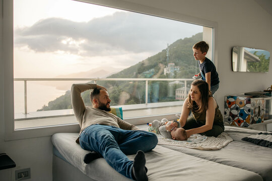 Family relaxing on beds in front of large window overlooking coastline - Powered by Adobe