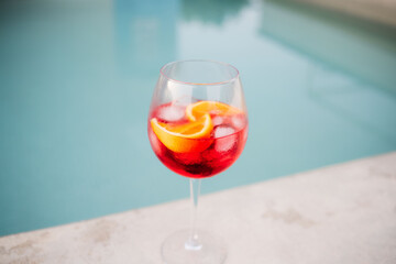Red cocktail with orange slices and ice cubes by the turquoise poolside