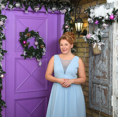 A woman in a light blue dress stands in front of a purple door decorated with a Christmas wreath